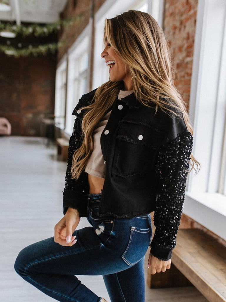 Black sequin sleeved jean jacket. Luxe combination of black sequins and denim. Button up, front pockets with frayed detail.