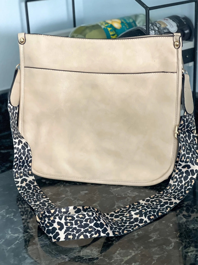 Ivory Crossbody bag with leopard print strap. Made with vegan leather, it features a full zipper closure, an exterior back zip pocket, two open slip pockets, and a zipper pocket inside.