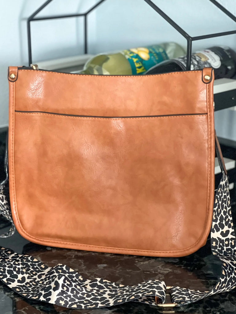 Brown Crossbody bag with leopard print strap. Made with vegan leather, it features a full zipper closure, an exterior back zip pocket, two open slip pockets, and a zipper pocket inside.