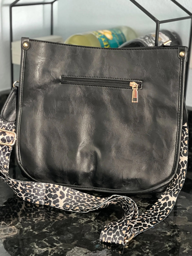 Black Crossbody bag with leopard print strap. Made with vegan leather, it features a full zipper closure, an exterior back zip pocket, two open slip pockets, and a zipper pocket inside.