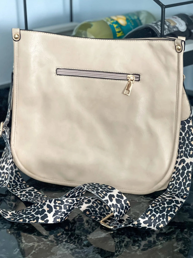 Ivory Crossbody bag with leopard print strap. Made with vegan leather, it features a full zipper closure, an exterior back zip pocket, two open slip pockets, and a zipper pocket inside.