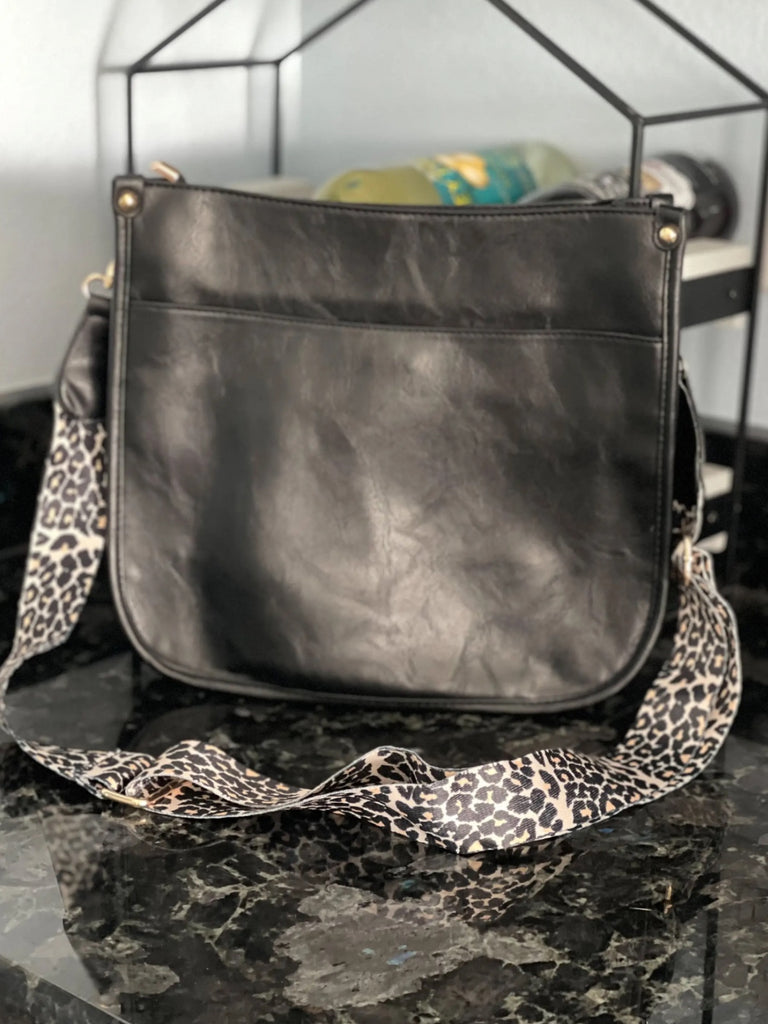 Black Crossbody bag with leopard print strap. Made with vegan leather, it features a full zipper closure, an exterior back zip pocket, two open slip pockets, and a zipper pocket inside.