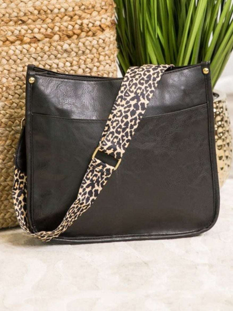 Black Crossbody bag with leopard print strap. Made with vegan leather, it features a full zipper closure, an exterior back zip pocket, two open slip pockets, and a zipper pocket inside.